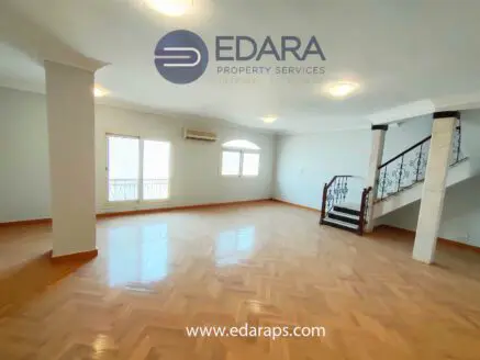 Interior view of a spacious room featuring a staircase and large windows allowing natural light.