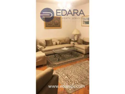 Living room featuring a beige sofa set, a glass coffee table, and a decorative rug on wooden flooring.