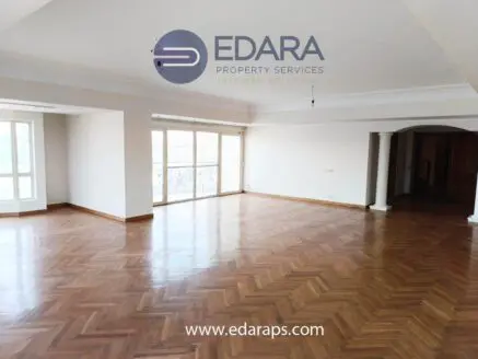 Bright and spacious living room featuring wooden herringbone flooring and large windows for natural light.