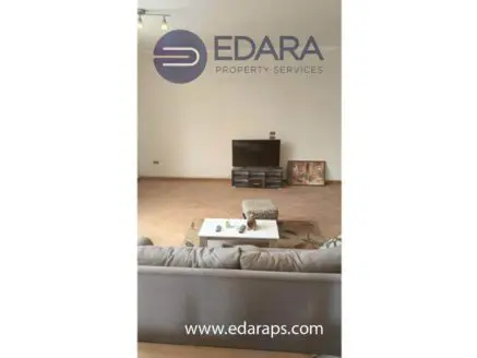 Living room featuring a sofa, television unit, and wooden flooring in a neutral color scheme.