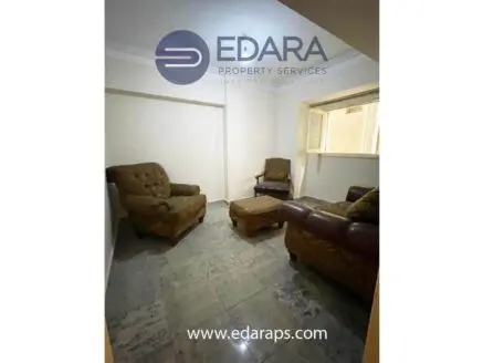 Seating area with two armchairs and an ottoman in a well-lit room with tiled flooring.