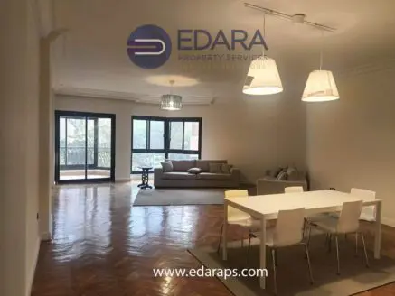 Spacious living room with a sofa, dining table, and large windows allowing natural light.