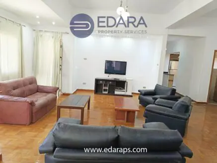 Living room featuring a brown couch, black armchairs, and a coffee table with a television in the background.