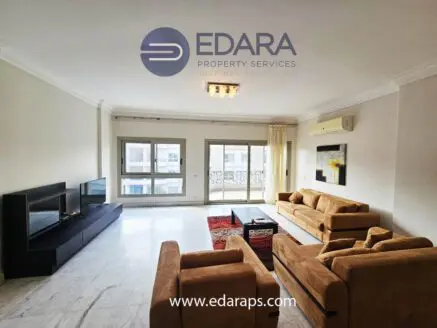 Spacious modern living room with beige sofas, a black coffee table, and a television unit against a white wall.