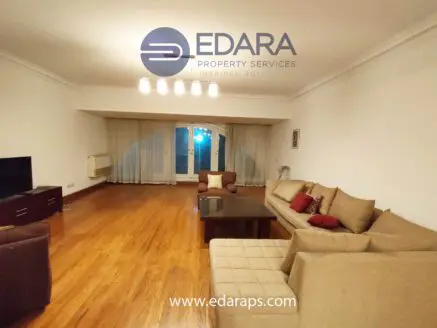 Spacious living room featuring a beige sofa set and a television unit against a wooden floor.