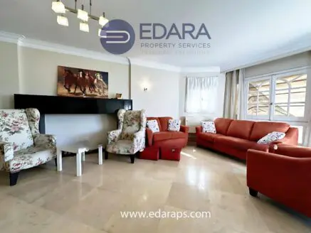 Living room featuring red sofas and floral patterned armchairs arranged around a fireplace.