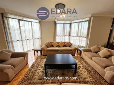 Living room featuring beige sofas arranged around a black coffee table on a patterned rug.