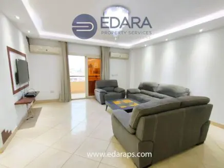 Modern living room featuring gray sofas, a television, and natural light from a balcony.