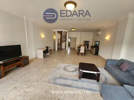 Living room featuring a sofa, coffee table, television, and dining area in a modern apartment.