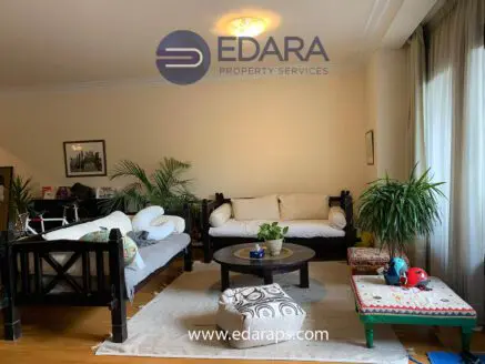 Living room featuring a wooden sofa, coffee table, and indoor plants in a bright setting.