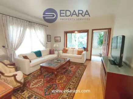Living room featuring white sofas, a decorative rug, and a television unit in a well-lit space.