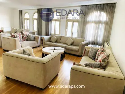 A spacious living room featuring beige sofas with floral cushions arranged around a central coffee table.