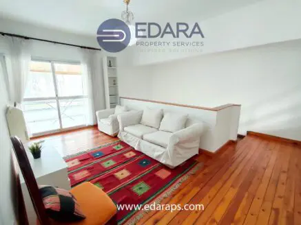 Living room featuring white sofas, a colorful rug, and wooden flooring in a well-lit space.