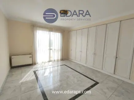 Bright interior room featuring a large window and built-in wardrobes against a light-colored wall.