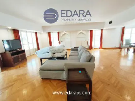 Living room featuring a large sofa, television, and natural light from windows.