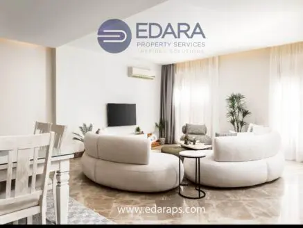 Contemporary living room featuring a curved sofa, coffee table, and decorative plants in a neutral color scheme.