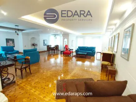Spacious living room featuring blue sofas and a brown armchair on a wooden floor.