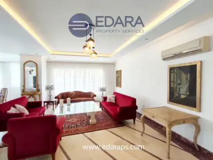 Living room featuring red sofas, a decorative rug, and a wooden table with art pieces.