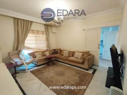 Living room featuring a beige sofa, decorative cushions, and a television on a stand.