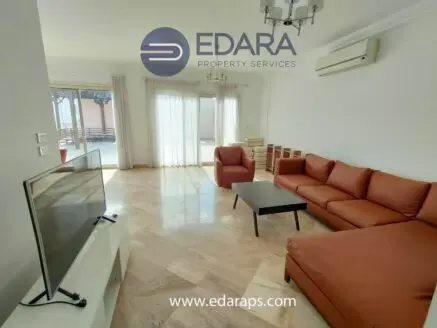 Modern living room featuring a brown leather sofa, television, and large windows with natural light.