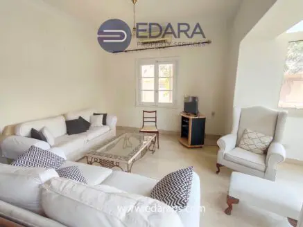 Bright living room featuring a white sofa set, coffee table, and a chair with decorative cushions.