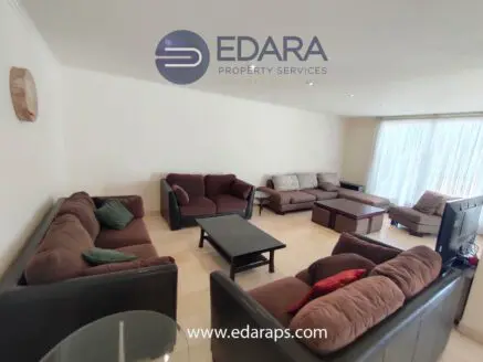Spacious living room featuring brown sofas, a coffee table, and a television setup.