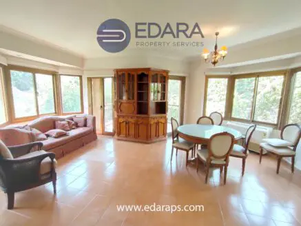 Spacious living room featuring a wooden cabinet, dining table, and seating area with a sofa and chairs.