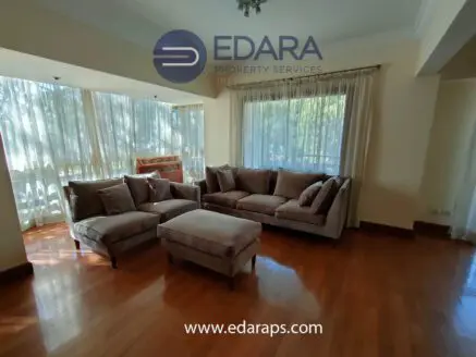 Spacious living room featuring a plush sofa set and an ottoman on polished wooden flooring.