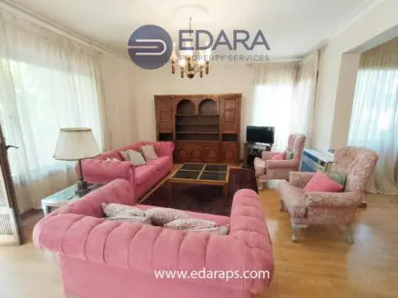 Living room featuring a pink sofa set with armchairs and a wooden bookshelf in a well-lit space.