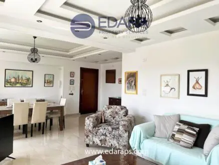 Interior view of a living room featuring a sofa, armchair, dining area, and wall art.