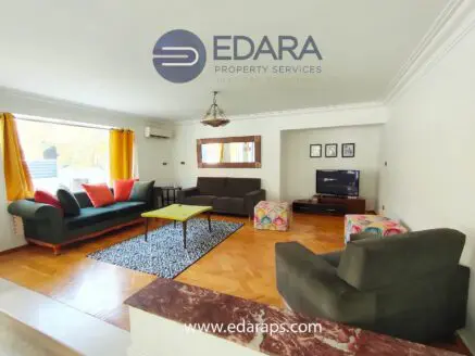 Spacious living room featuring a sofa set, coffee table, and television in a well-lit environment.