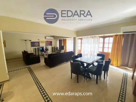 Interior view of a spacious living room featuring a dining table and seating area with large windows.