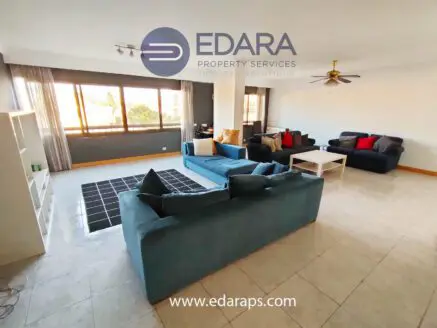 Bright living room featuring multiple sofas, a coffee table, and large windows allowing natural light.