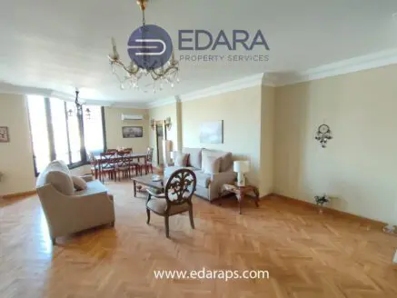 Spacious living room featuring beige sofas, a dining area, and wooden flooring.
