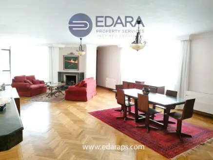 Spacious living room featuring red sofas, a dining table, and hardwood flooring with a fireplace.