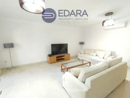 Living room featuring a light-colored sofa, wooden TV stand, and a flat-screen television.