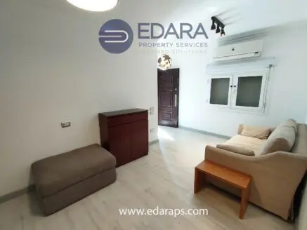 Living room featuring a beige sofa, wooden side table, and a storage ottoman in a bright indoor space.