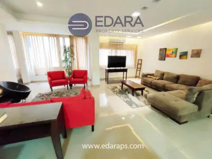 Living room featuring red armchairs, a beige sofa, and a television stand with a TV.