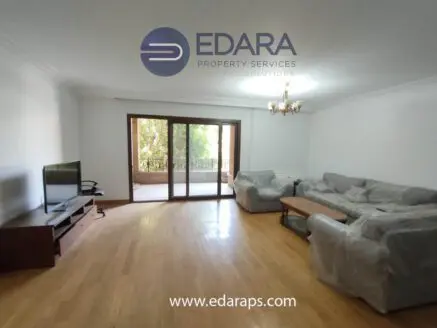 Spacious living room featuring a sofa set, television, and large windows for natural light.