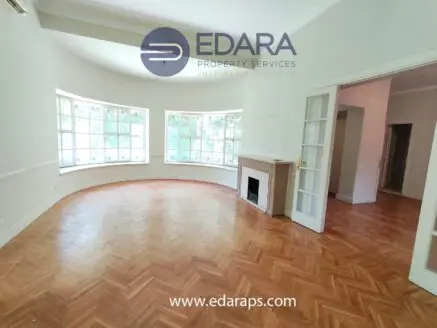Interior view of a spacious room featuring large windows and herringbone wooden flooring.