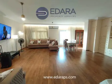 Bright living room featuring a large sofa, dining table, and wall-mounted television in a modern interior design.