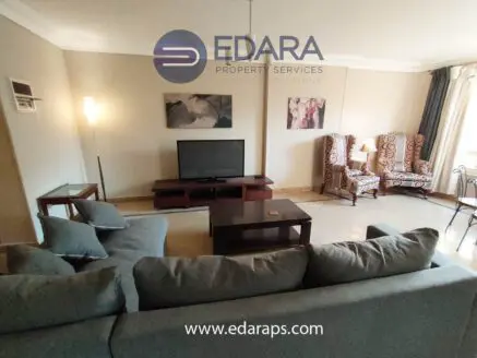 Spacious living room featuring a gray sectional sofa and a flat-screen television on a wooden stand.