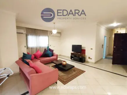 Living room featuring a pink sofa with colorful cushions and a television on a stand.