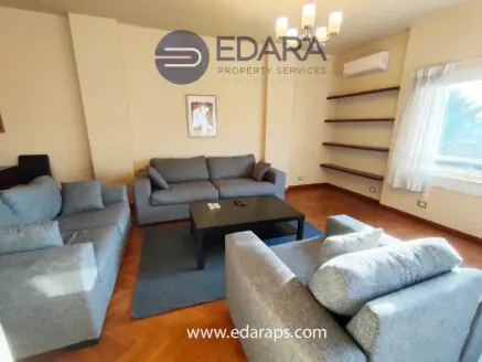 Living room featuring gray sofas arranged around a black coffee table with a wall-mounted shelf.