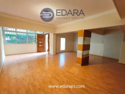 Interior view of a spacious room with wooden flooring and large windows allowing natural light.
