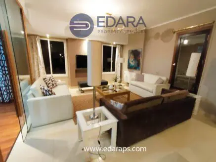 Contemporary living room with white sofas, a coffee table, and a television in a well-lit space.