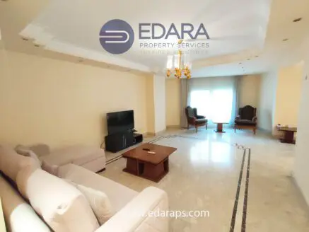 Spacious living room featuring a light-colored sofa, coffee table, and two armchairs near a large window.