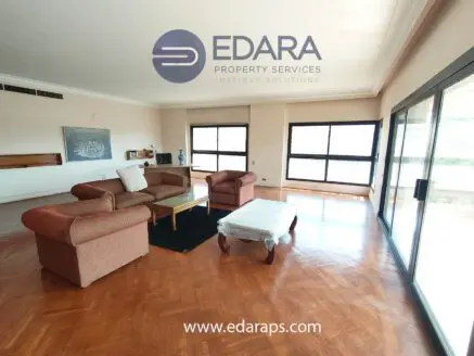 Bright living room featuring a large sofa set and a coffee table with a view through large windows.