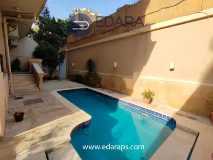 Residential swimming pool with tiled edges and surrounding plants in a well-lit area.