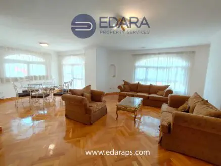 Spacious living room featuring a sofa set and a dining table with chairs, illuminated by natural light.